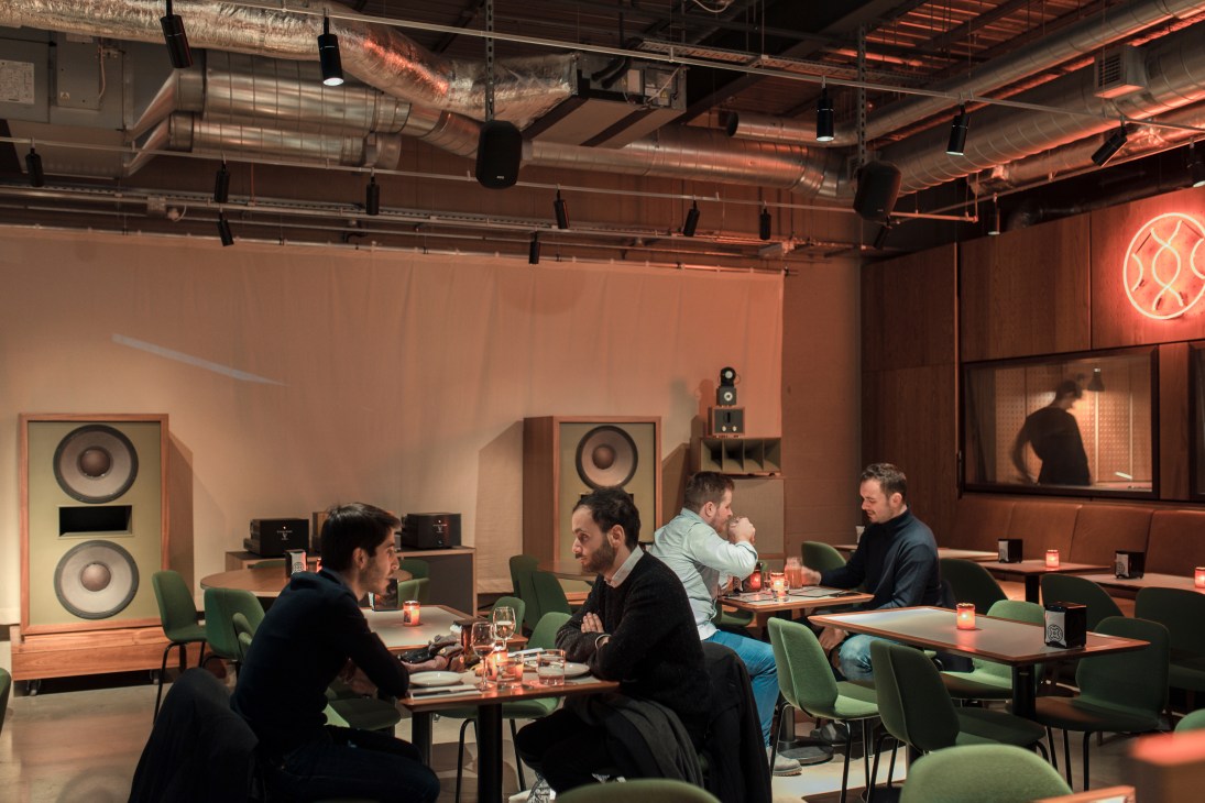 Spiritland's interior with diners at tables, large speaker systems, and warm orange-tinted lighting.